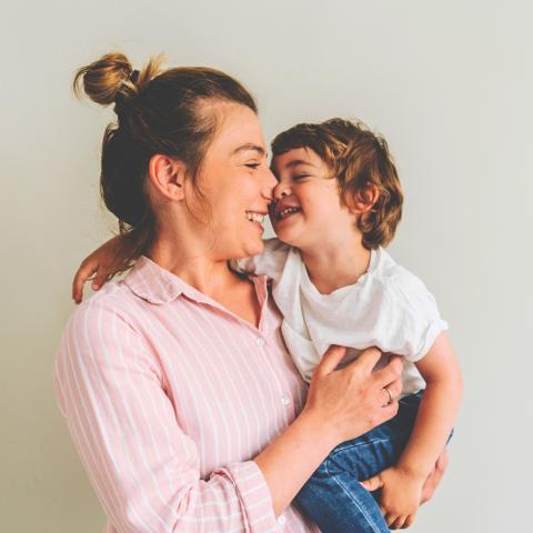 Mother smiling and holding her young child as they touch noses affectionately.